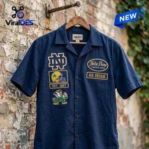 Front view of a navy blue Notre Dame Fighting Irish camp Hawaiian shirt hanging on a wooden hanger against a brick wall.