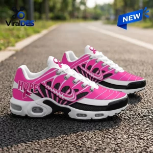 Outdoor view of pink and white Air Max Plus sneakers featuring hope text and ribbon motifs.