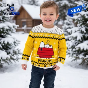 Front view of a smiling child wearing a Peanuts Snoopy Yellow Christmas Ugly Sweater outdoors in the snow.