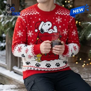 Front view of a person wearing a red and white Peanuts Snoopy Holiday Ugly Sweater holding a mug.