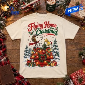 Front view of a cream t-shirt with a Snoopy Woodstock Flying Home Christmas graphic on a wooden table.