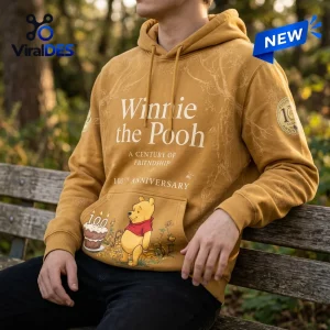 Front view of a person wearing the Winnie the Pooh 100th Anniversary yellow hoodie on a bench.