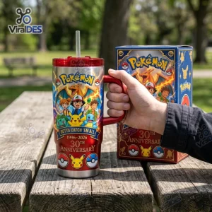 Hand holding a Pokemon Gotta Catch 'Em All 30th Anniversary Tumbler with straw on a wooden picnic table.