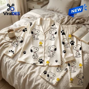 Top view of a personalized Snoopy cartoon satin pajama set laid flat on a bed.
