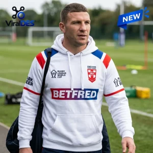 Man wearing an England Rugby World Cup 2026 white hoodie with sponsor logos at an outdoor sports field.