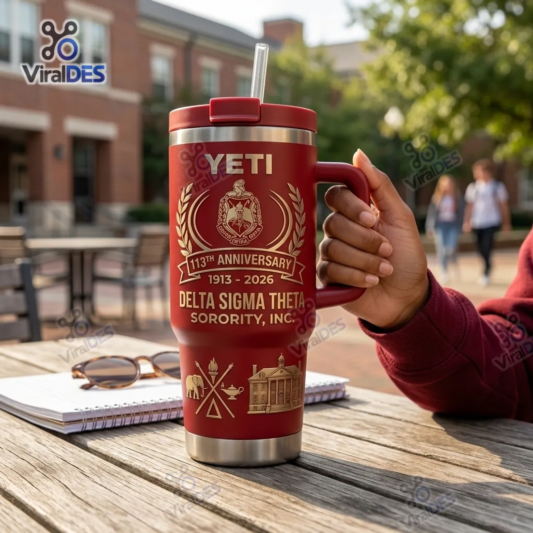 Hand gripping the crimson handle of the Delta Sigma Theta 113th Anniversary YETI Tumbler Cup on an outdoor campus table