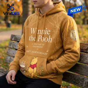 Front view of a Winnie the Pooh 100th Anniversary yellow hoodie worn on a park bench.
