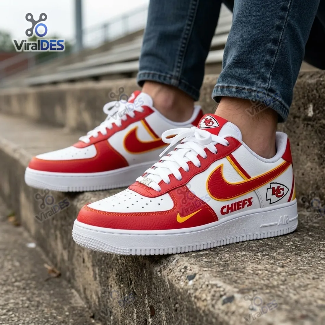 Close-up on-foot view of the Kansas City Chiefs Nike Air Force 1 Sneakers on concrete steps highlighting the perforated white toe box, KC tongue tag, and stitched white rubber sole