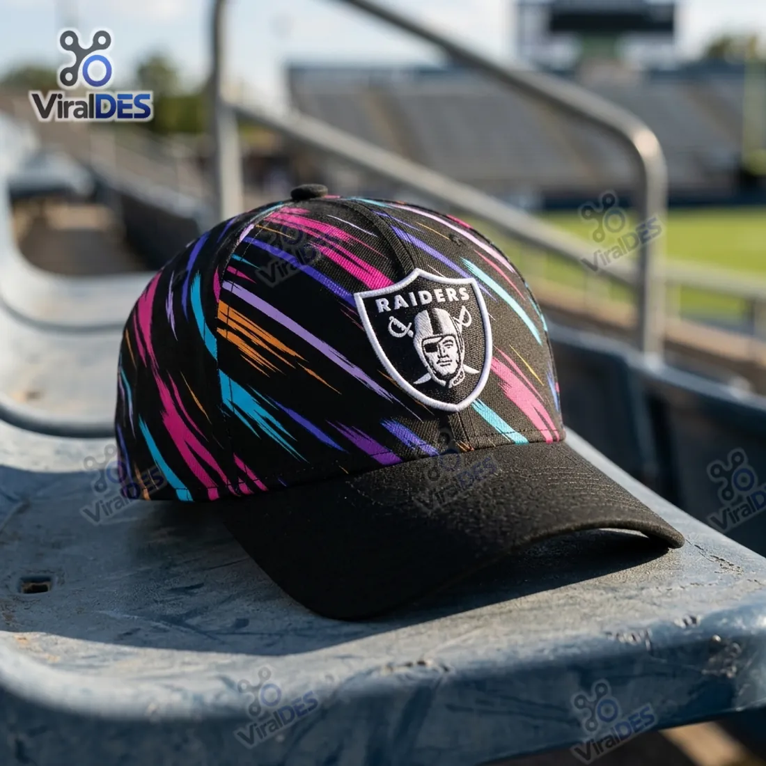 Las Vegas Raiders NFL Crucial Catch 2026 Black Cap resting on metal stadium bleachers featuring diagonal multicolor brushstrokes and the Raiders shield