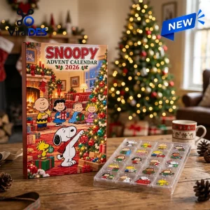 Front view of a Snoopy Peanuts Christmas advent calendar box next to a tray of pins on a wooden table.