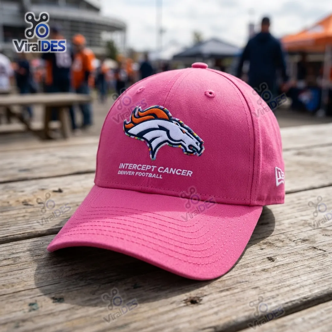 NFL Crucial Catch Denver Broncos Pink Cap resting on a wooden tailgate table outside the stadium showing the Broncos logo and Intercept Cancer text