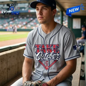 Man wearing the Cleveland Guardians Take October 2026 Gray Baseball Jersey sitting in a stadium dugout.