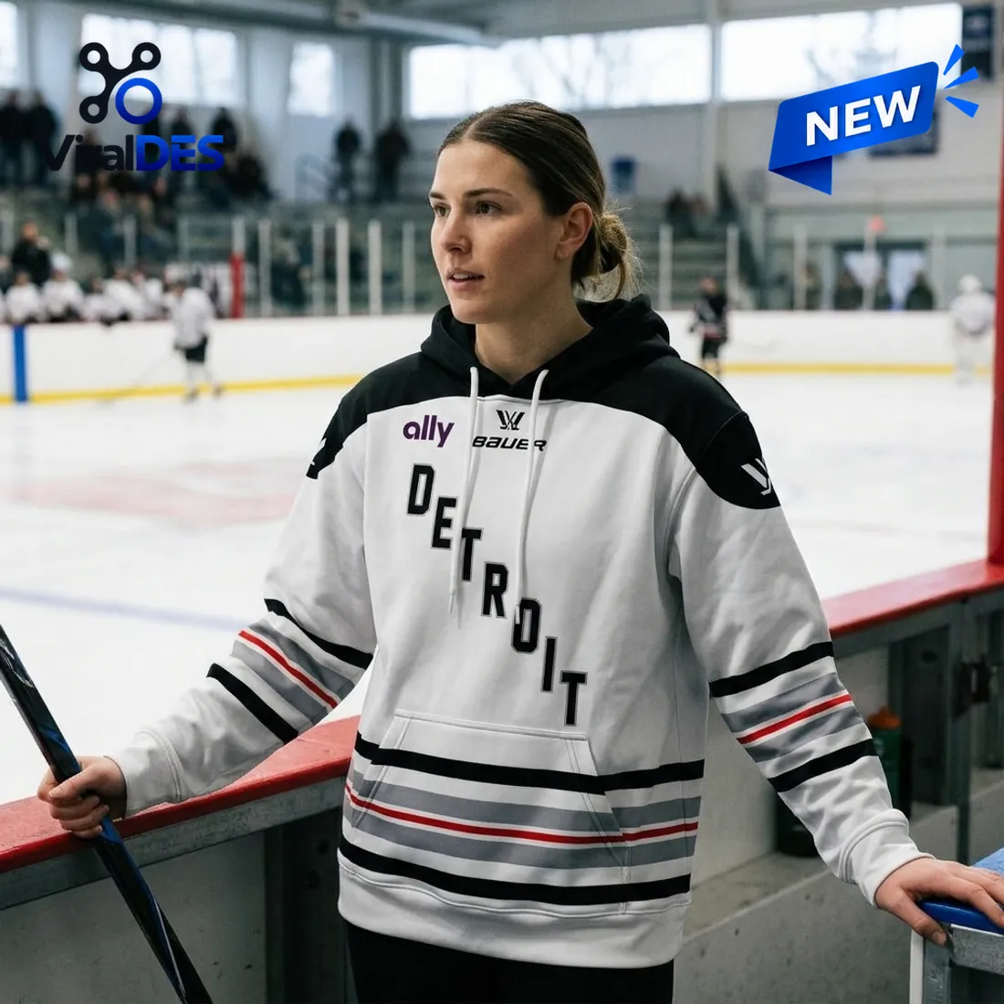 Rinkside boards view of the PWHL Detroit 2026 Away Hoodie held with a hockey stick showing the sleeve and kangaroo pocket striping