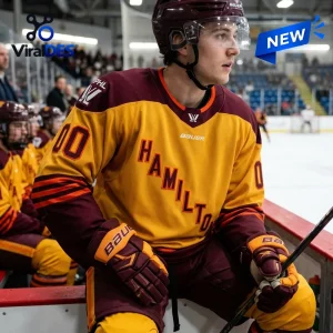 Player wearing gold and maroon PWHL Hamilton 2026 hockey jersey sitting on bench.