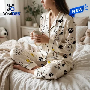 Side angle of woman wearing personalized satin pajama set with cartoon graphic print while holding a ceramic mug on a bed.