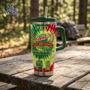 Front view of a Mountain Dew 86th Anniversary Tumbler Cup sitting on an outdoor wooden table in a forest setting.